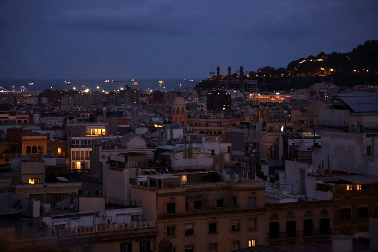 Barcelona's rooftops at night, with lit windows down to the sea.