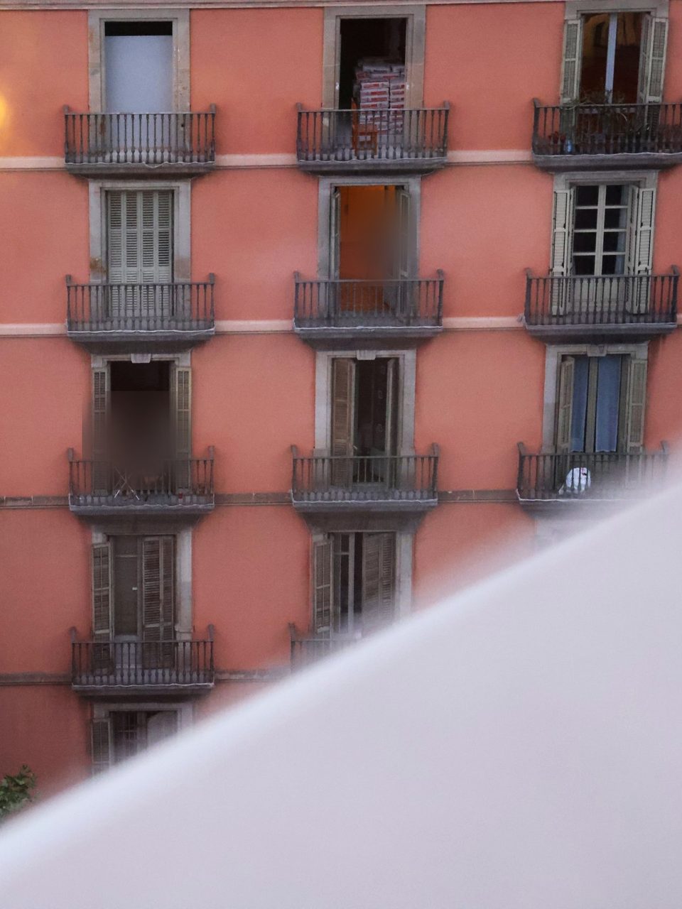 A lit window and balconies on a pink facade at dusk.